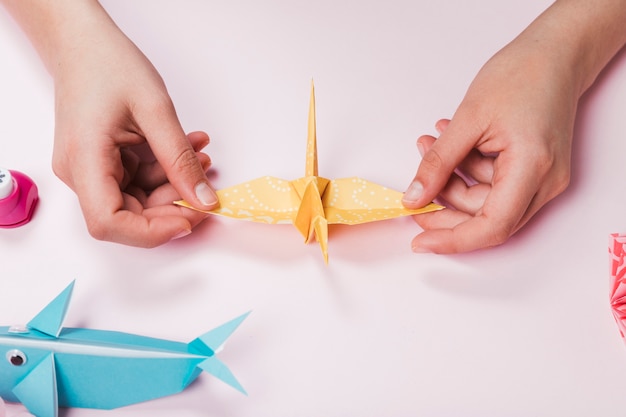 Female hand made bird from origami paper on pink backdrop