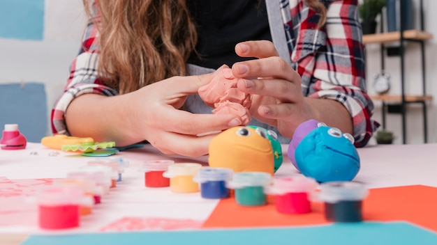 Женская рука делает мультяшные лица с использованием разноцветной глины