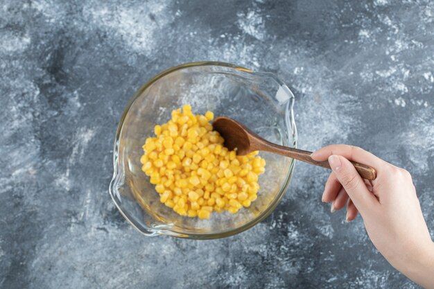 Female hand mixing sweet corns in glass bowl.