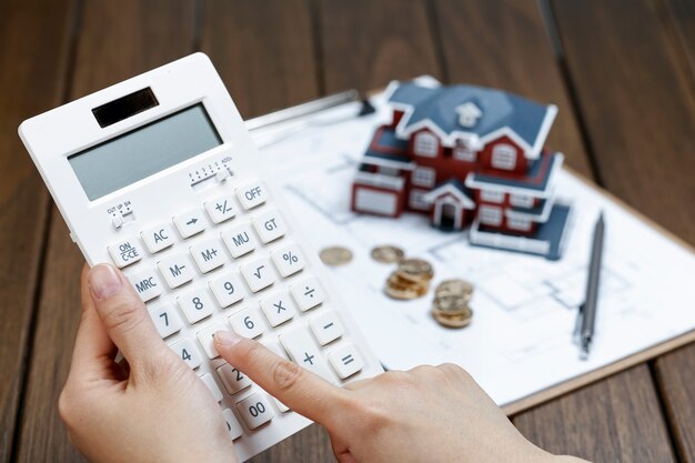 A female hand operating a calculator in front of a villa house model Free Photo