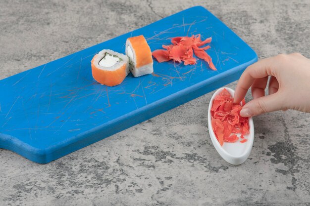 Female hand picking pickled ginger from blue cutting board