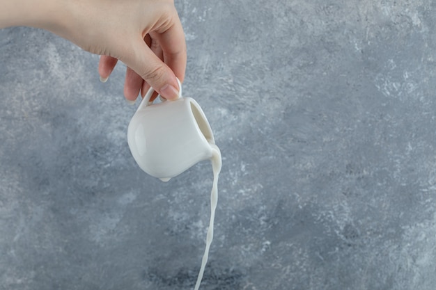 Free photo female hand pouring fresh milk out of small mug.