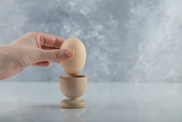 Женская рука принимая вареное яйцо из яичной чашки на белом фоне.