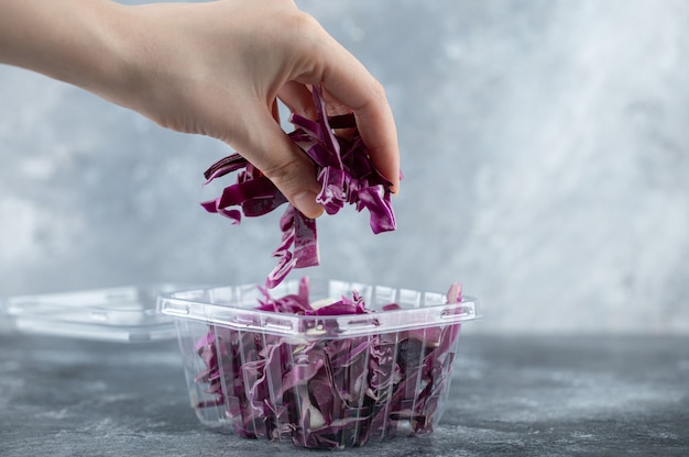 Female hand taking chopped cabbage from plastic container. 