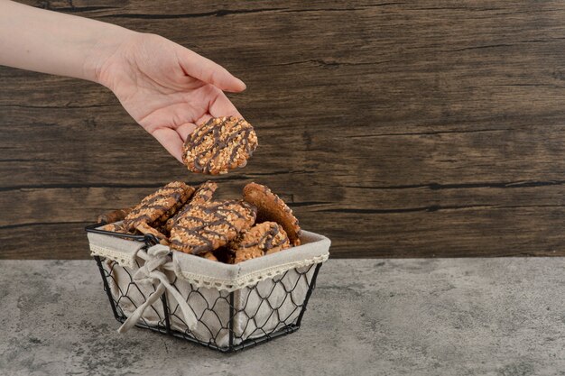 Female hand taking fresh baked cookies from basket on marble surface.