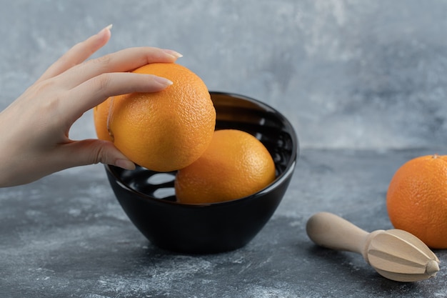 黒のボウルから新鮮なオレンジを取る女性の手。