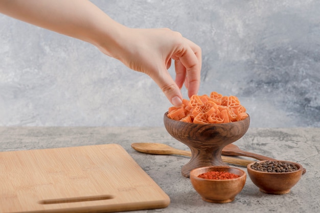 Free photo female hand taking macaroni from wooden bowl on marble background