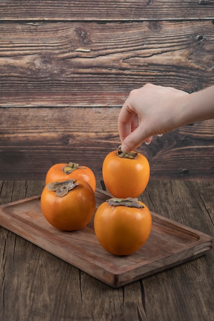 Free photo female hand taking single persimmon fruit on wooden surface