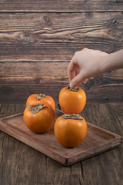 female hand taking single persimmon fruit on wooden surface