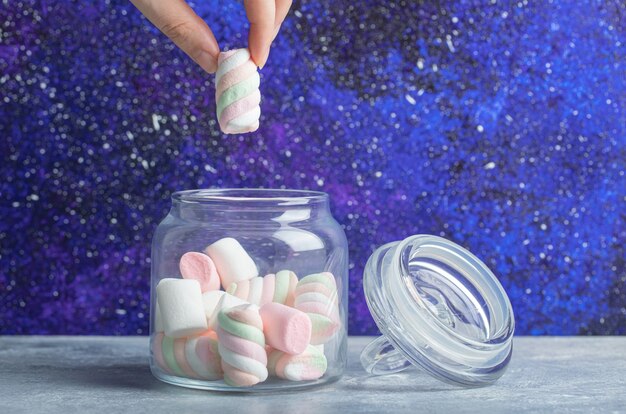 Free photo female hand taking soft colorful marshmallows out of glass jar