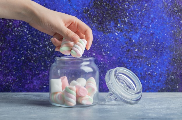 Free photo female hand taking soft colorful marshmallows out of glass jar