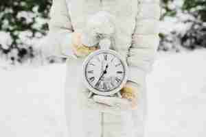 Foto gratuita la mano femminile in un bianco ha tricottato i guanti che tengono i grandi orologi sul fondo dell'inverno