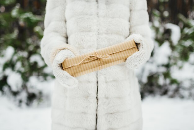 Female hand in a white knitted mittens holding present gift box 