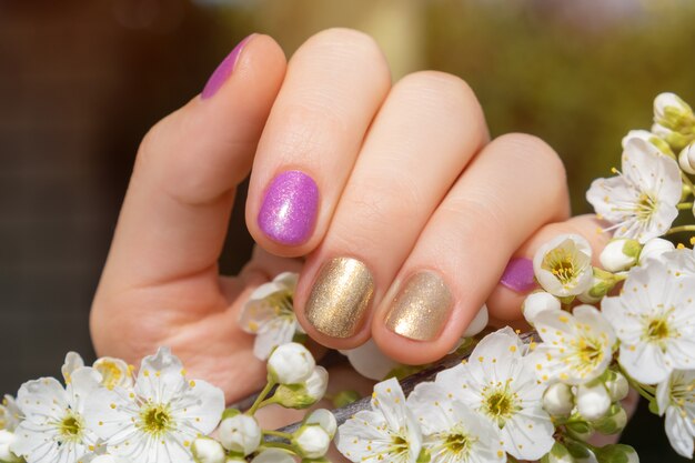 Female hand with gold and purple nail design holding blossom cherry branch.