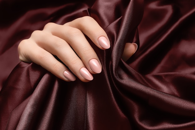 Женская рука с розовым дизайном ногтей на поверхности темной ткани. Premium Фотографии