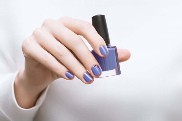 Женская рука с фиолетовым дизайном ногтя держит бутылку лака для ногтей