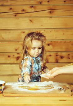 Женские руки помогают ребенку готовить с тестом, мукой, яйцом, миской