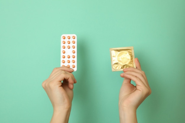 Female hands hold condom and pills on mint wall