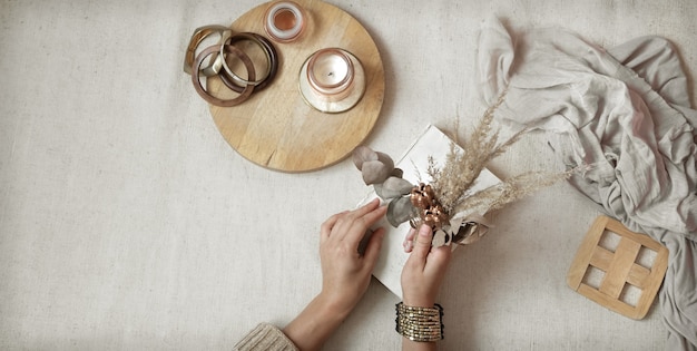 Female hands hold dried flowers with wooden decor details, copy space and top view.