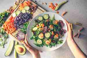 無料写真 新鮮な野菜とビーガン サラダのボウルを保持している女性の手の上面図