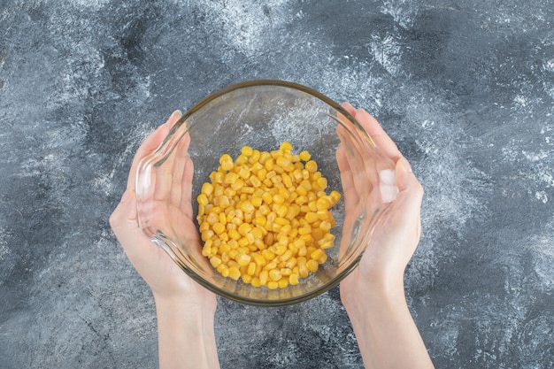 Female hands holding bowl of canned corns on marble.