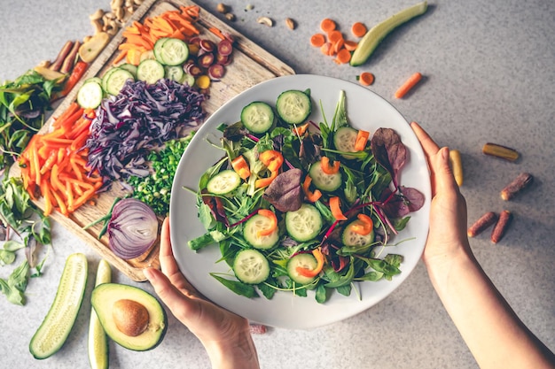 Mani femminili che tengono una ciotola di insalata vegana con vista dall'alto di verdure fresche