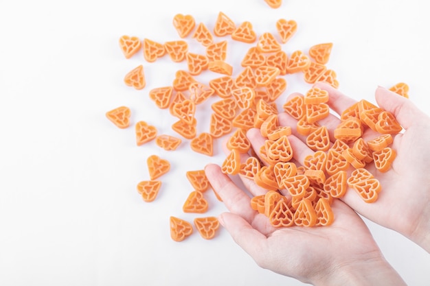 Female hands holding bunch of raw heart shaped pasta on white.