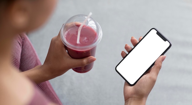 Female hands holding a fruit juice and smartphone with a blank screen