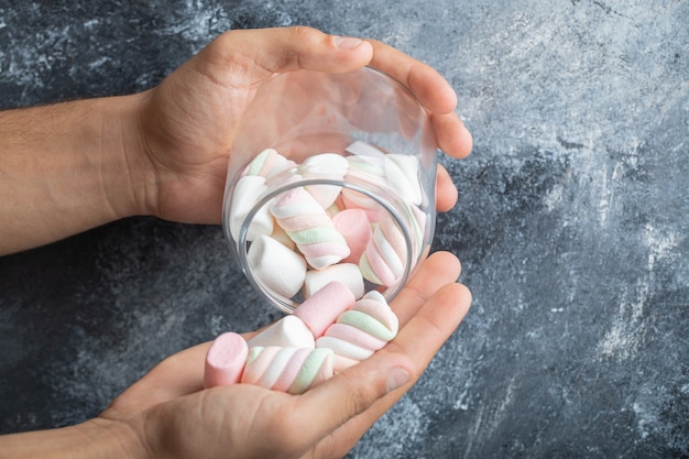 Female hands holding glass jar of marshmallows on marble background