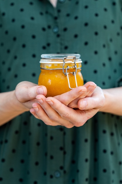 Mani femminili che tengono una marmellata di albicocche cruda vegana fatta in casa in un barattolo di vetro