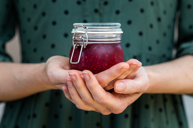 Female hands holding a homemade vegan raw raspberry jam in a glass jar