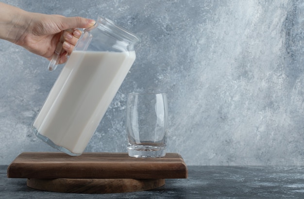 Free photo female hands holding jug of milk on marble.