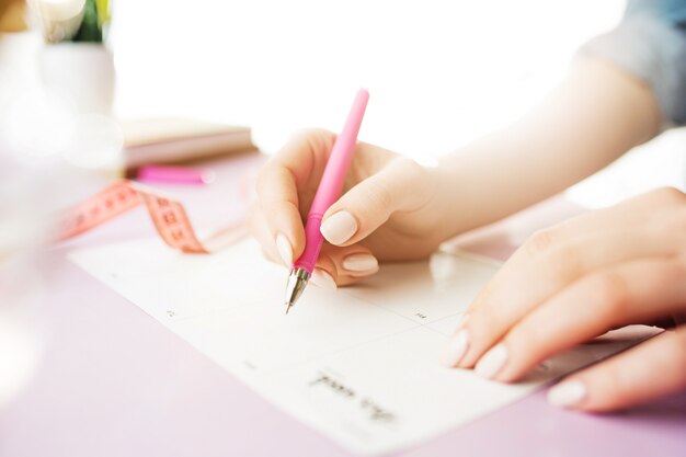 ペンを持つ女性の手。トレンディなピンクのデスク。