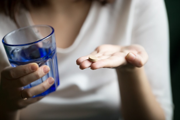 Female hands holding pill and glass of water, closeup view