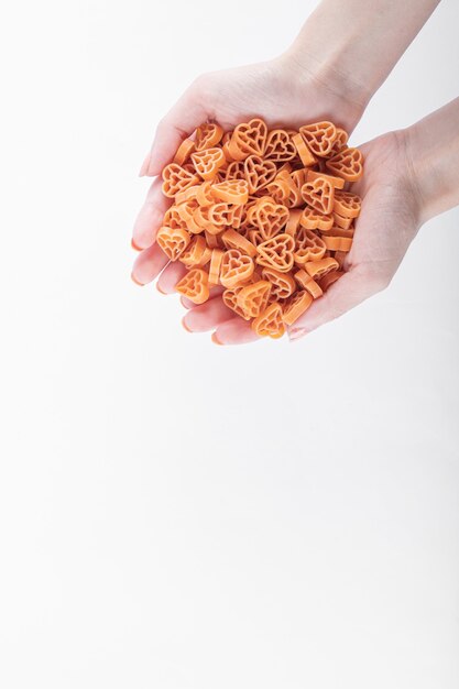Female hands holding raw heart shaped pasta on white background. High quality photo