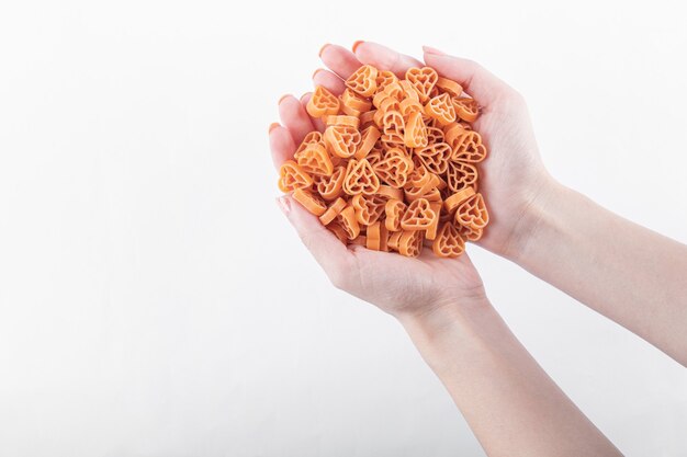 Female hands holding raw heart shaped pasta on white.
