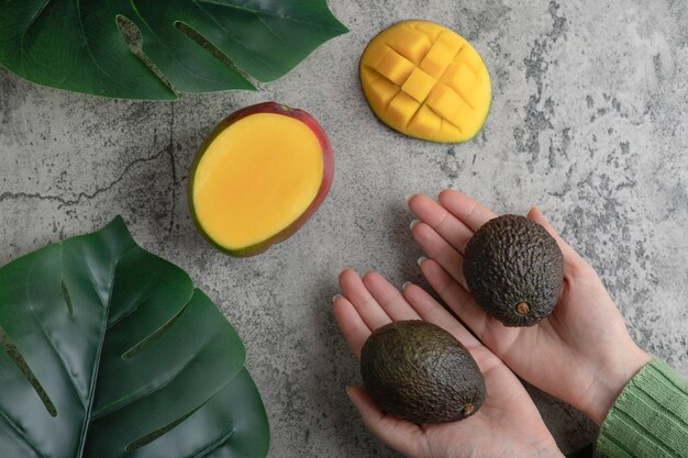 Женские руки, держа спелые авокадо на мраморной поверхности.