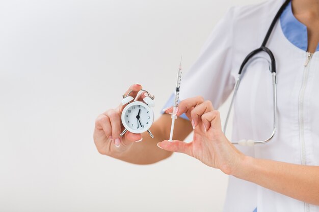 Free photo female hands holding a syringe and a clock