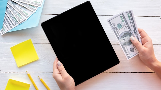 Female hands holding a tablet and money. Finance idea