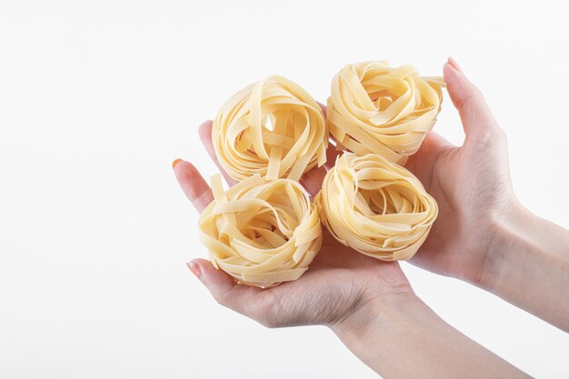 Female hands holding tagliatelle nests on white.