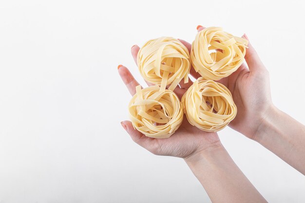 Female hands holding tagliatelle nests on white.