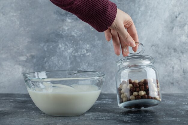 Female hands holding tip of glass jar with cereal balls.