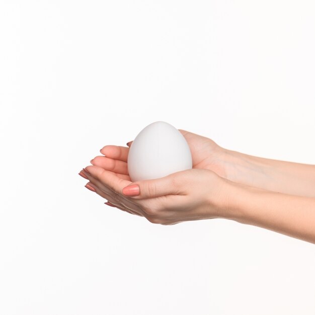 Женские руки держат белое яйцо на белом.
