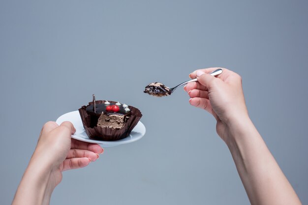 Female hands keeping cake with spoon on gray