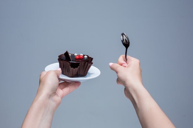 Female hands keeping cake with spoon on gray