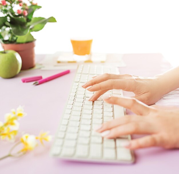 Женские руки на клавиатуре. Вид сбоку на женщину. Стол модного розового цвета.