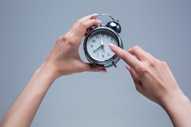 The female hands and old style alarm clock on gray