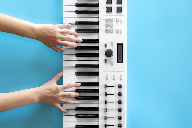 Женские руки играют музыкальные клавиши на синем фоне, вид сверху