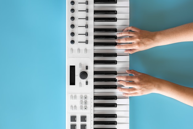 Female hands play on white musical keys on a blue background, top view, minimalism, copy space.