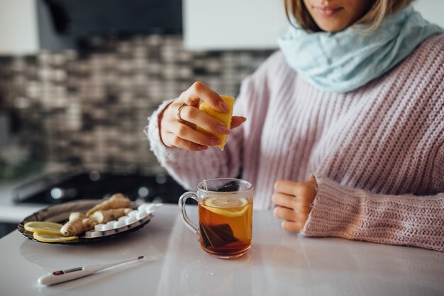 Female hands squeezing lemon to her tea.